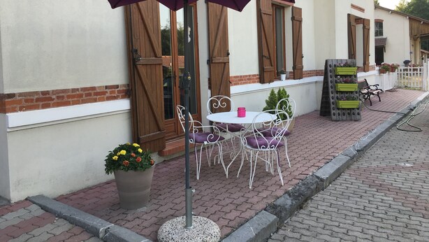 Ulkoterassi, jossa on violetti aurinkovarjo, valkoiset metallituolit ja pöytä.