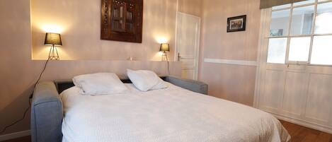 A bedroom with a bed, two bedside lamps, a wooden headboard, a door, and a window with blinds.