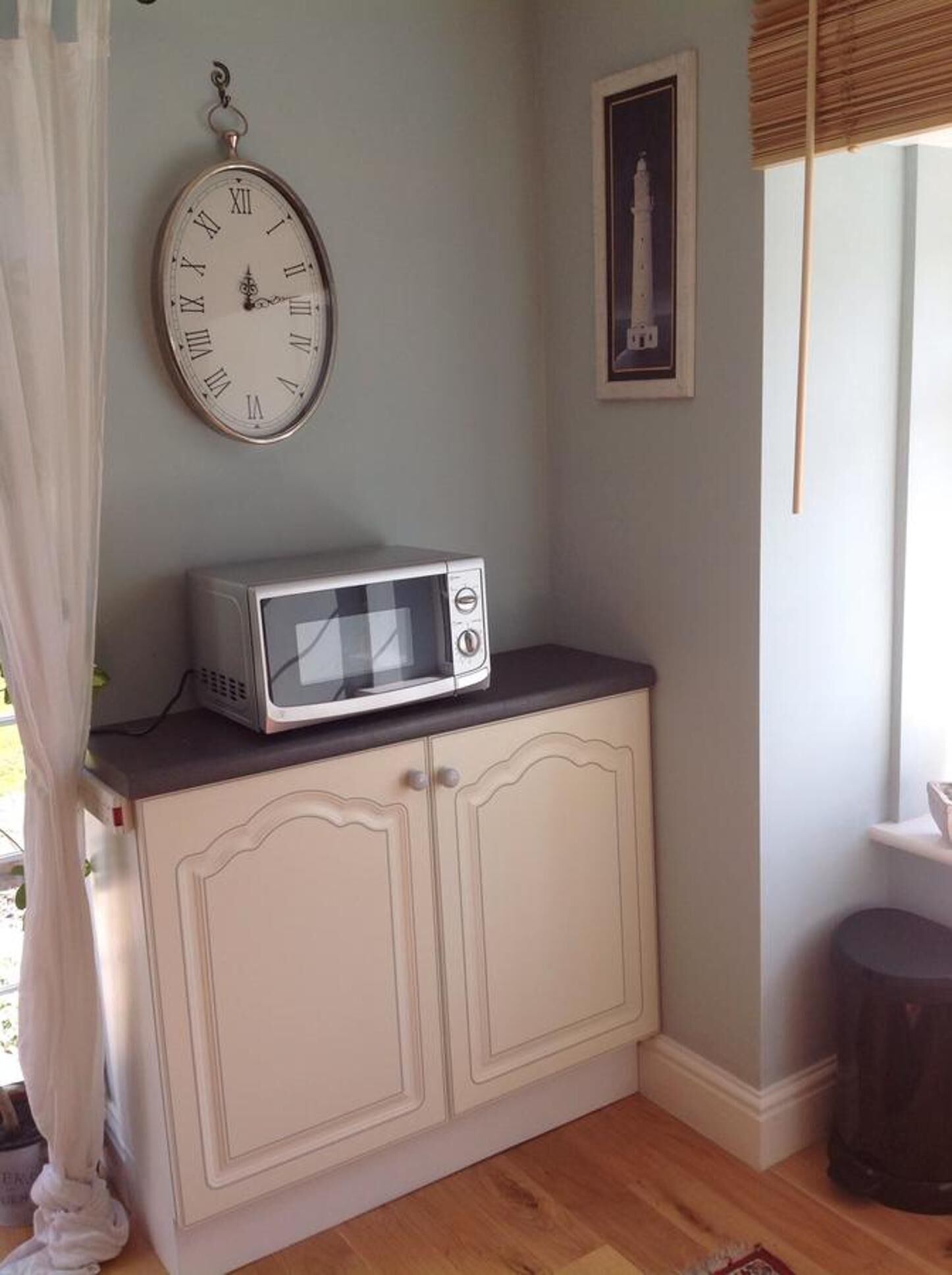 Una cocina con un microondas sobre un mueble, un reloj en la pared y un cuadro enmarcado encima del microondas.