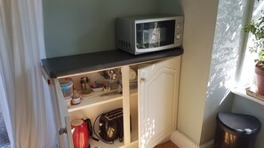 A compact kitchen with a microwave on the counter, a toaster, and various kitchen utensils and dishes in the cabinets. - The Summer Room (Norwich)