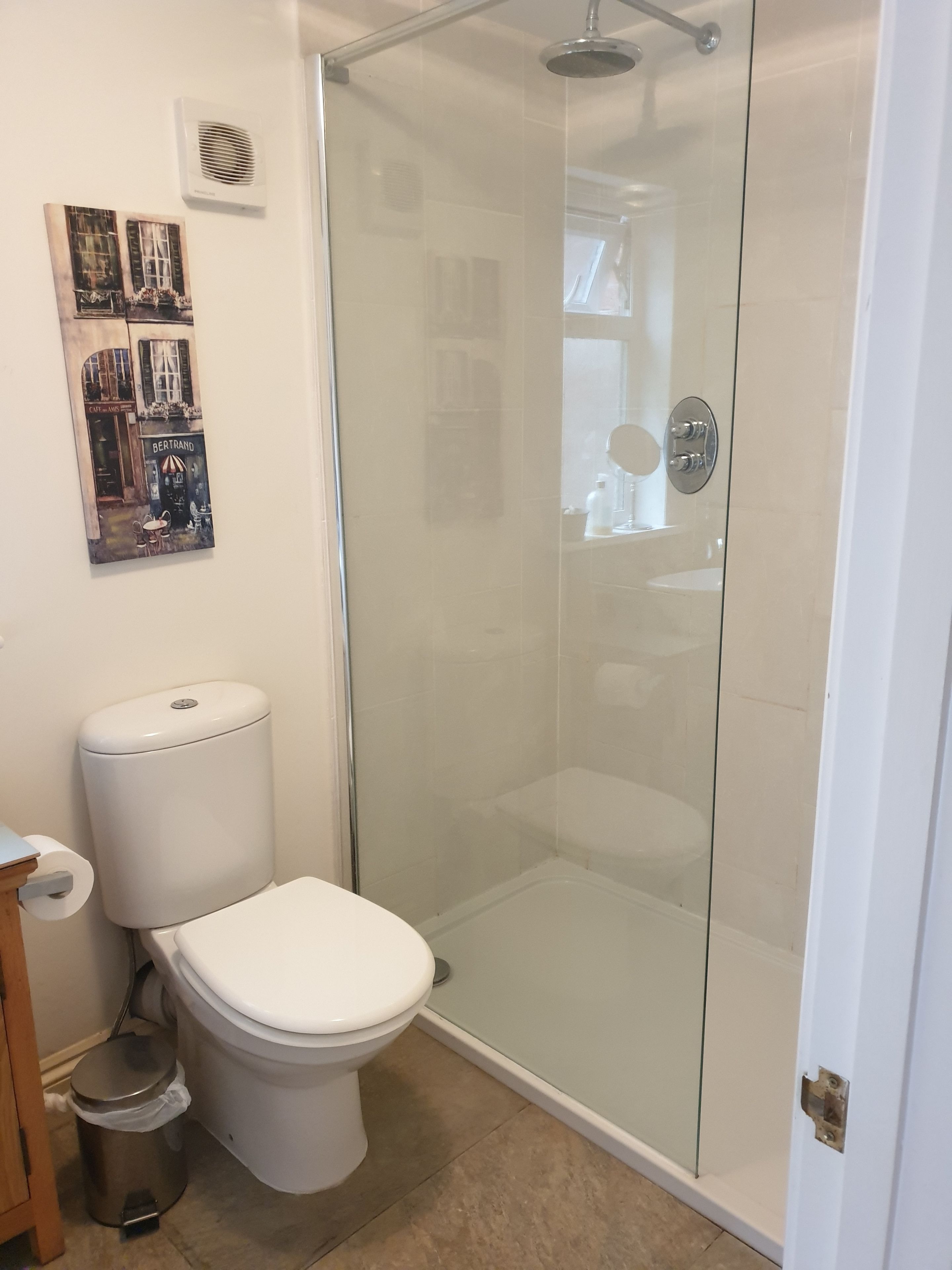 Une salle de bain avec une douche à parois de verre, des toilettes et une poubelle.