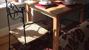 A dining area with a wooden table, two chairs, a potted plant, and a window with a view of greenery. - The Summer Room (Norwich)