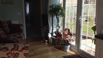 A cozy living room with a floral-patterned sofa, a potted plant, and a view of a garden through large glass doors.