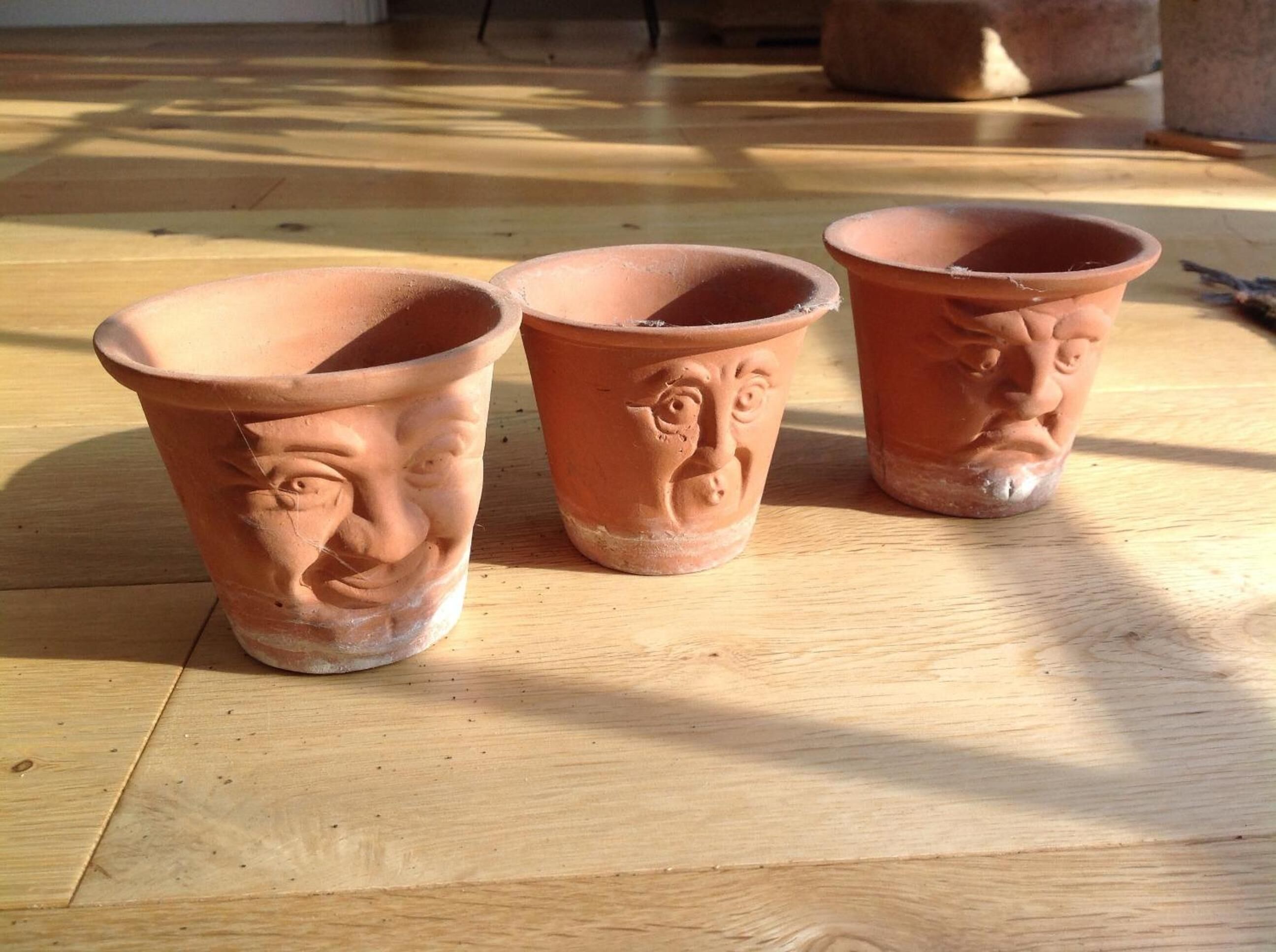 Three terracotta pots with embossed designs on a wooden floor.