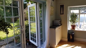 A room with a view of a garden, a small kitchen area with a microwave, and a potted plant by the window. - The Summer Room (Norwich)