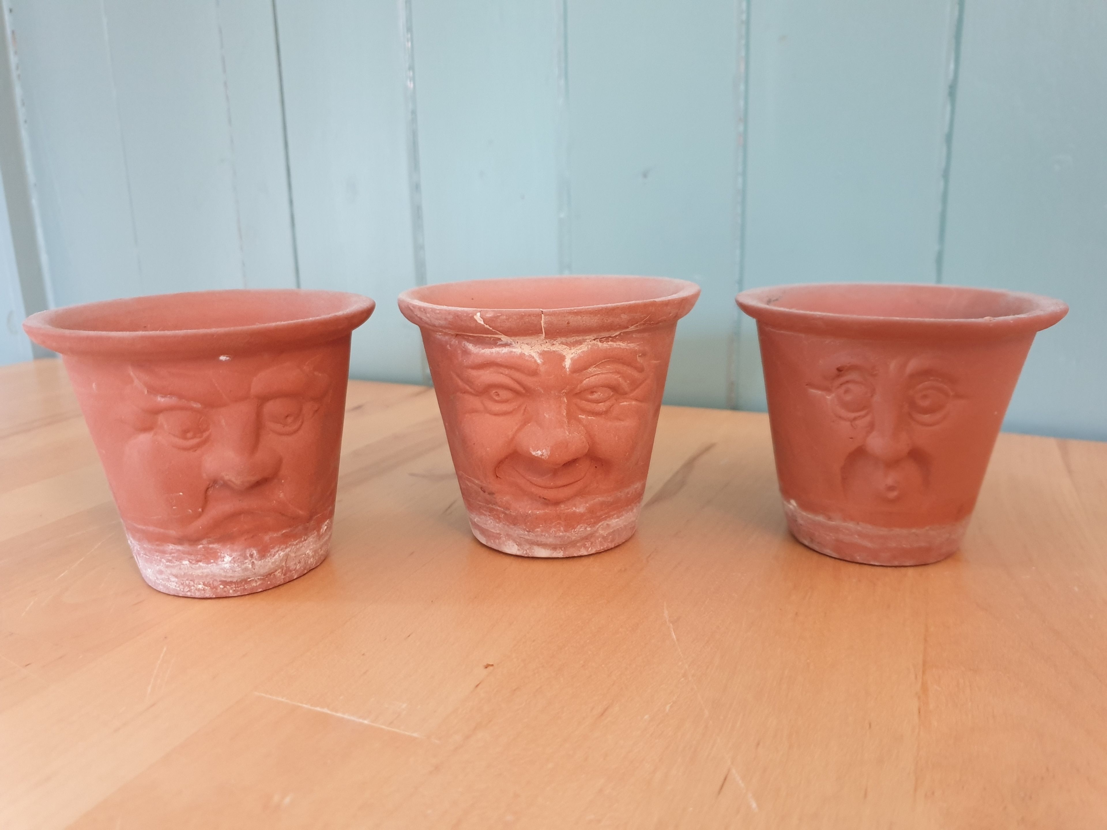 Three terracotta pots with faces on a wooden surface.