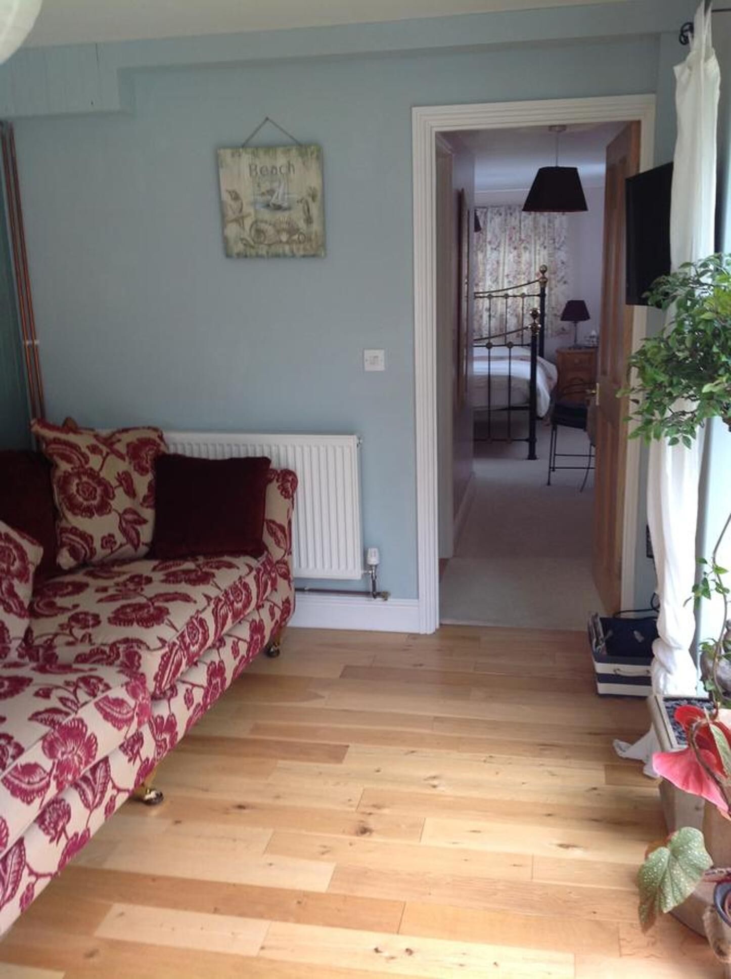Een kamer met een bed, een radiator, een houten vloer en een deur die naar een andere kamer leidt.
