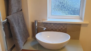 Ein Badezimmer mit einem weißen Waschbecken, einem Handtuchhalter, einem Fenster mit Milchglas und einem Holzschrank.