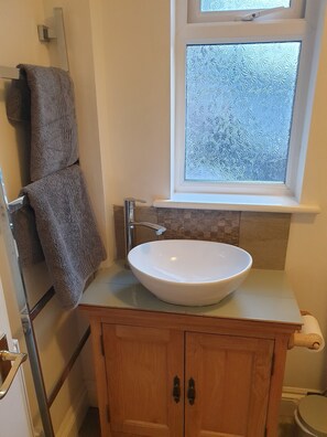 A bathroom with a white sink, a towel rack, a window with frosted glass, and a wooden cabinet. - The Summer Room (Norwich)