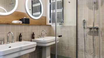 A modern bathroom with two sinks, a glass shower enclosure, and a mirror with a wooden shelf above.
