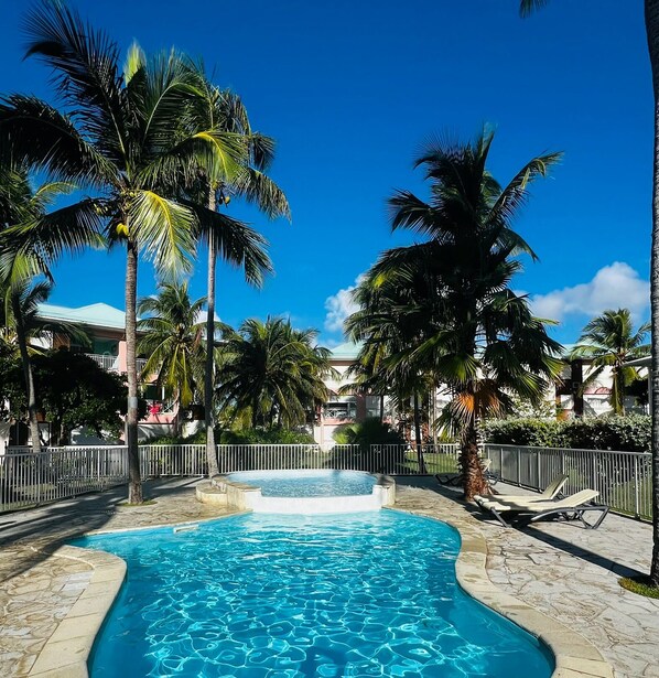 A swimming pool with clear blue water, surrounded by palm trees and a stone deck. - LM Crystal Beach Sea View & Direct Beach Access 💯 air-conditioned (SAINT-FRANCOIS)