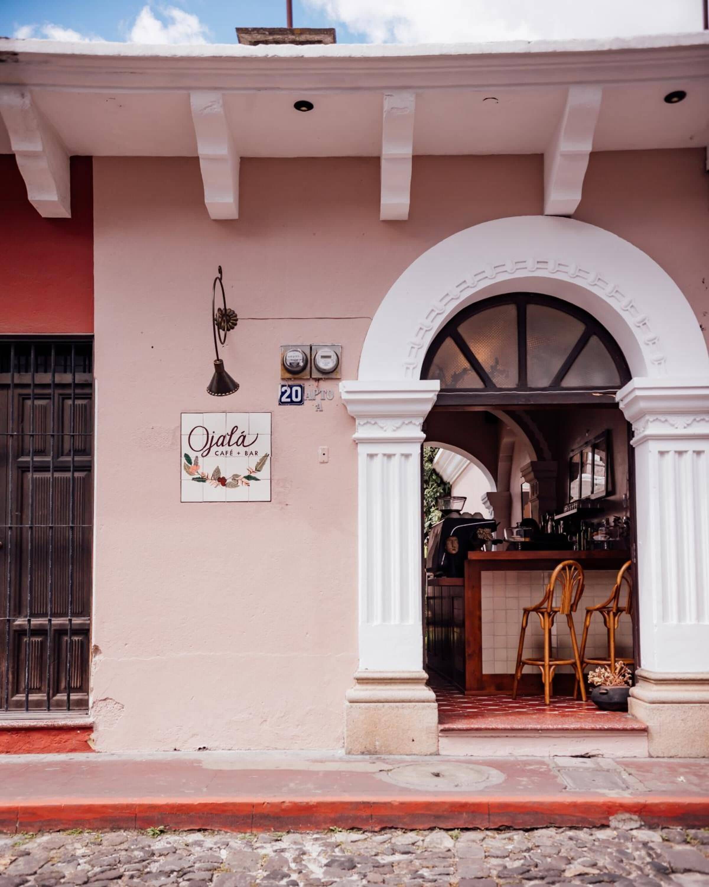 Un café appelé « Ojala », avec une enseigne, le numéro « 20 », et un coin bar avec des chaises.