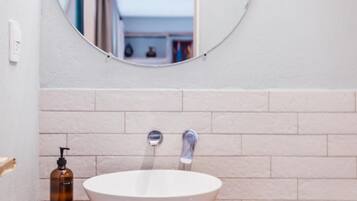 Ein Badezimmer mit Waschbecken, Holz-Waschtisch und rundem Spiegel.