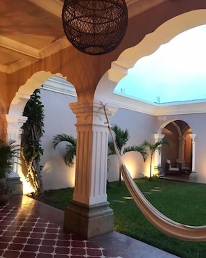 A covered courtyard with white columns, a hammock, and palm trees. - Ojala (Antigua Guatemala)