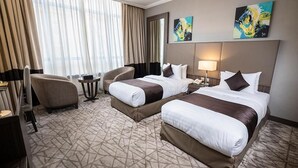 Une chambre d’hôtel avec deux lits, un bureau, une chaise, une petite table et une grande fenêtre avec des rideaux.