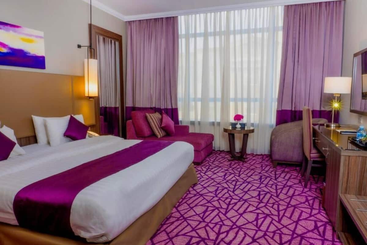 Une chambre d’hôtel avec un grand lit, un bureau, une chaise et une petite table avec une lampe.