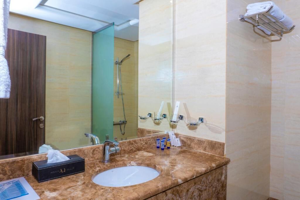 Un bagno con lavabo in marmo, uno specchio, un porta asciugamani e una zona doccia.