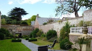 Une cour avec un sol en pierre, un espace détente avec des chaises, un palmier en pot et un mur en pierre.
