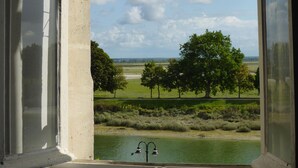 Une vue à travers une fenêtre, avec une structure en béton, une étendue d’eau et des arbres au loin.