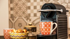 Eine Kaffeemaschine, eine Tasse Kaffee, eine Schale mit Biscotti und ein dekorativer Behälter auf einer Küchenarbeitsfläche.