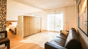 Ein modernes Hotelzimmer mit einem Holzschrank, einer Ledersofa, einem weißen Teppich und einem großen Fenster mit Jalousien.