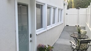A residential exterior with a white door, a 'hello' mat, a potted plant, and a small patio with a table and chairs.