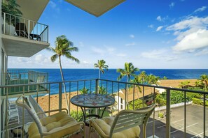 Un balcon avec vue sur la plage et l’océan, une table ronde et deux chaises.