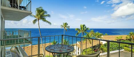 A balcony with a view of the beach and ocean, a round table, and two chairs.