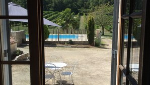 A view through a glass door of a patio area with a pool, a fenced garden, and a table with chairs.