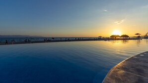 Vista a la piscina al atardecer, con cielo despejado, agua tranquila y montañas lejanas.