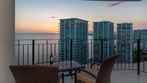 Un balcón con vista al mar y edificios altos al atardecer.
