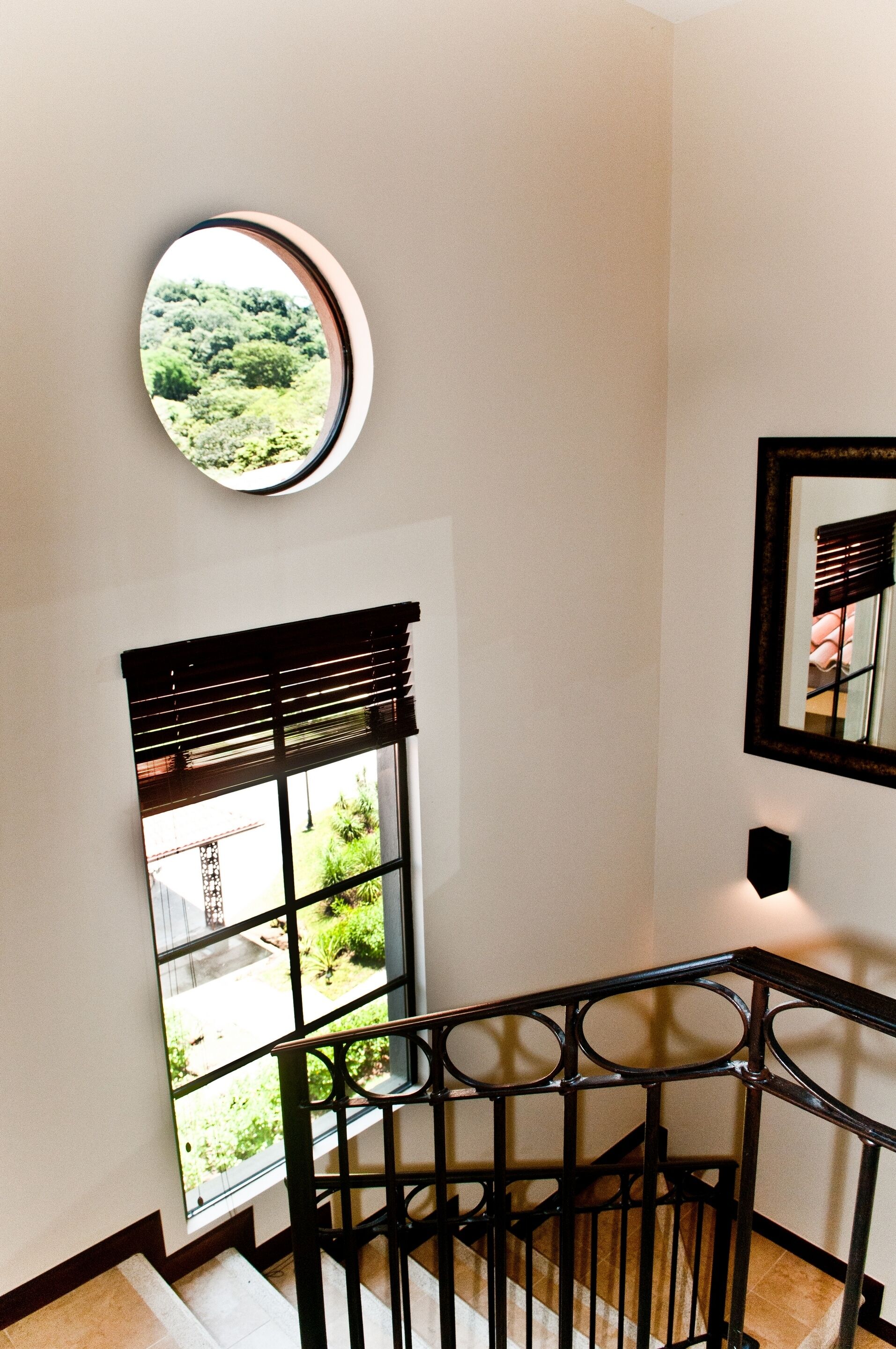 Una escalera con vistas a la vegetación a través de una ventana y un espejo redondo en la pared.