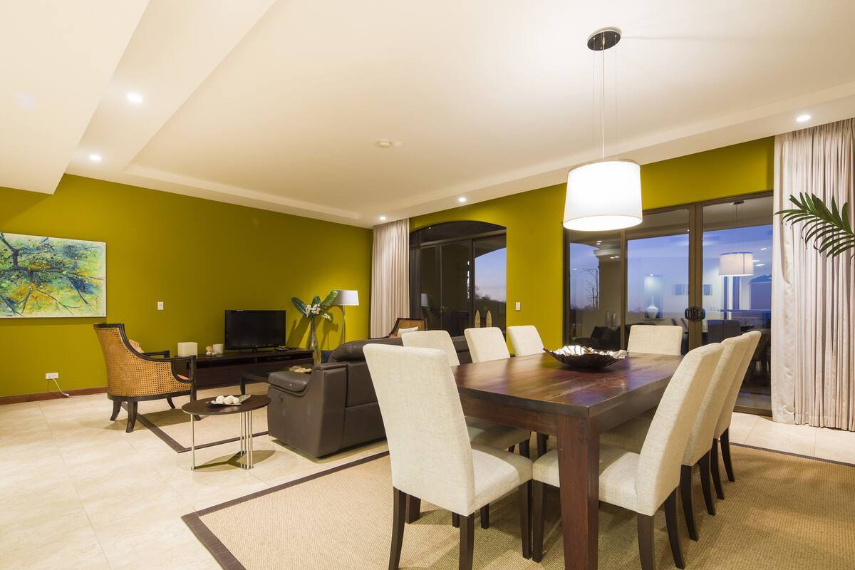 A modern living room with a dining area, a sofa, a TV, and a large window with curtains.
