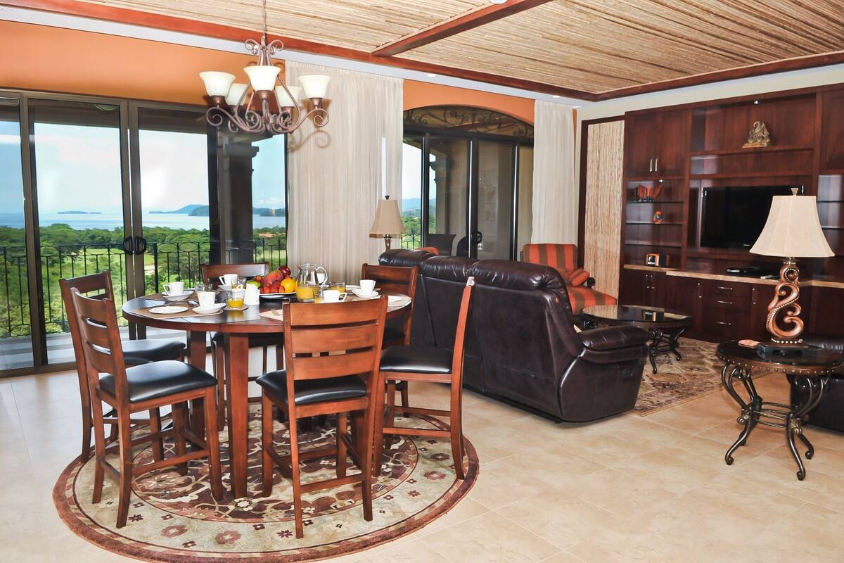 A spacious living area with a dining table, leather sofa, and a TV.