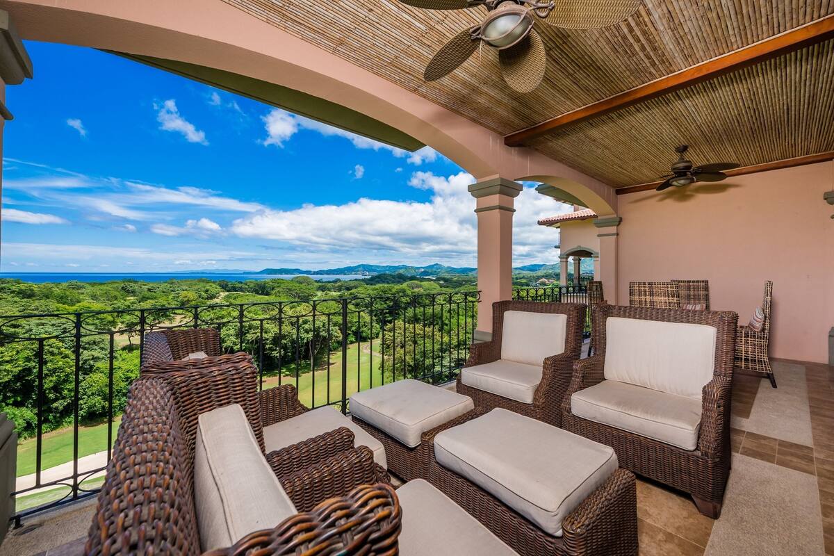 A balcony with wicker furniture, a ceiling fan, and a view of a lush landscape.
