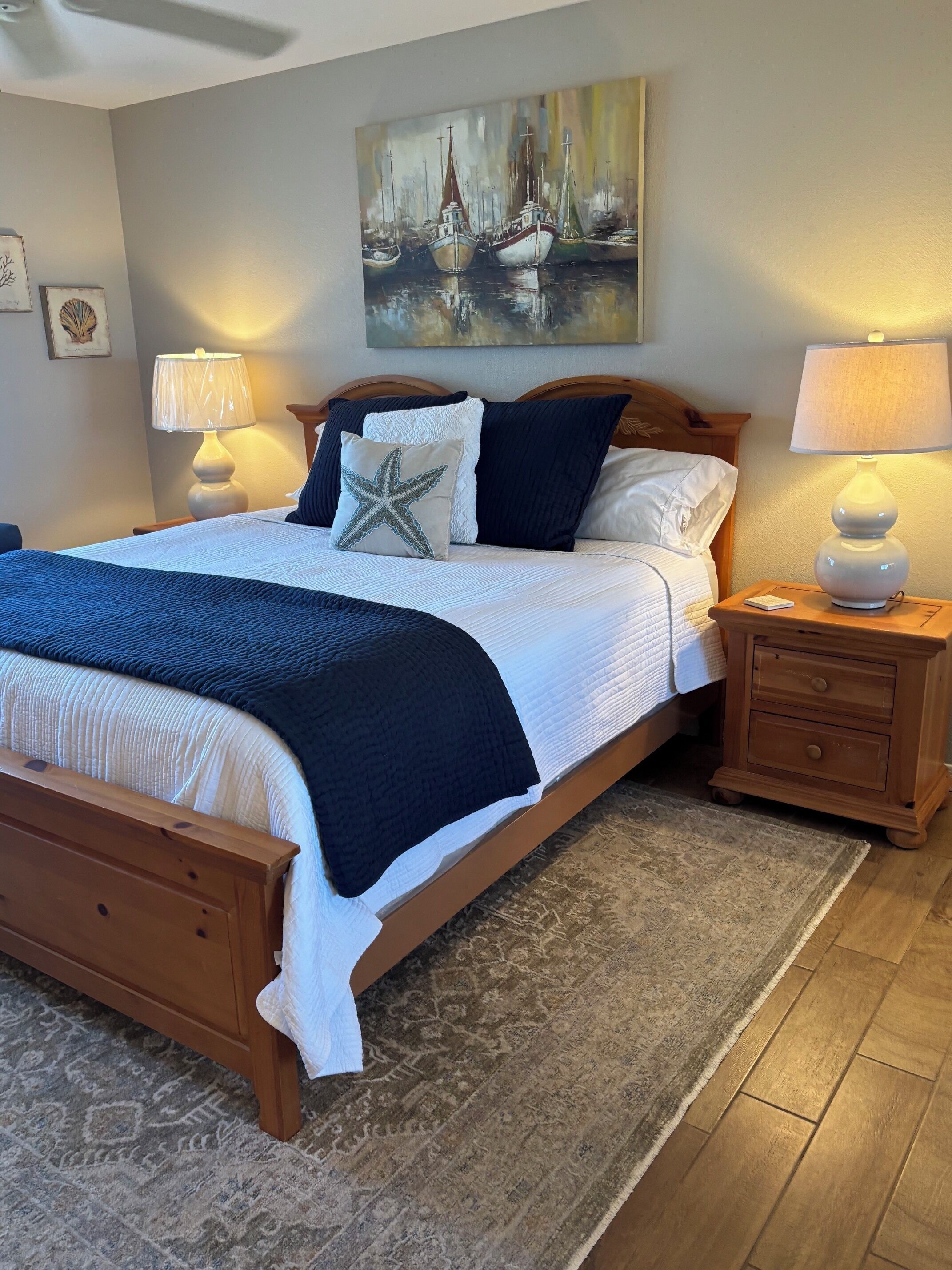 A neatly made bed with a star-shaped pillow, a wooden headboard, and a painting of boats on the wall.