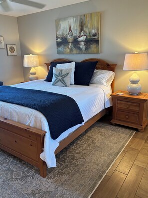 A neatly made bed with a star-shaped pillow, a wooden headboard, and a painting of boats on the wall.