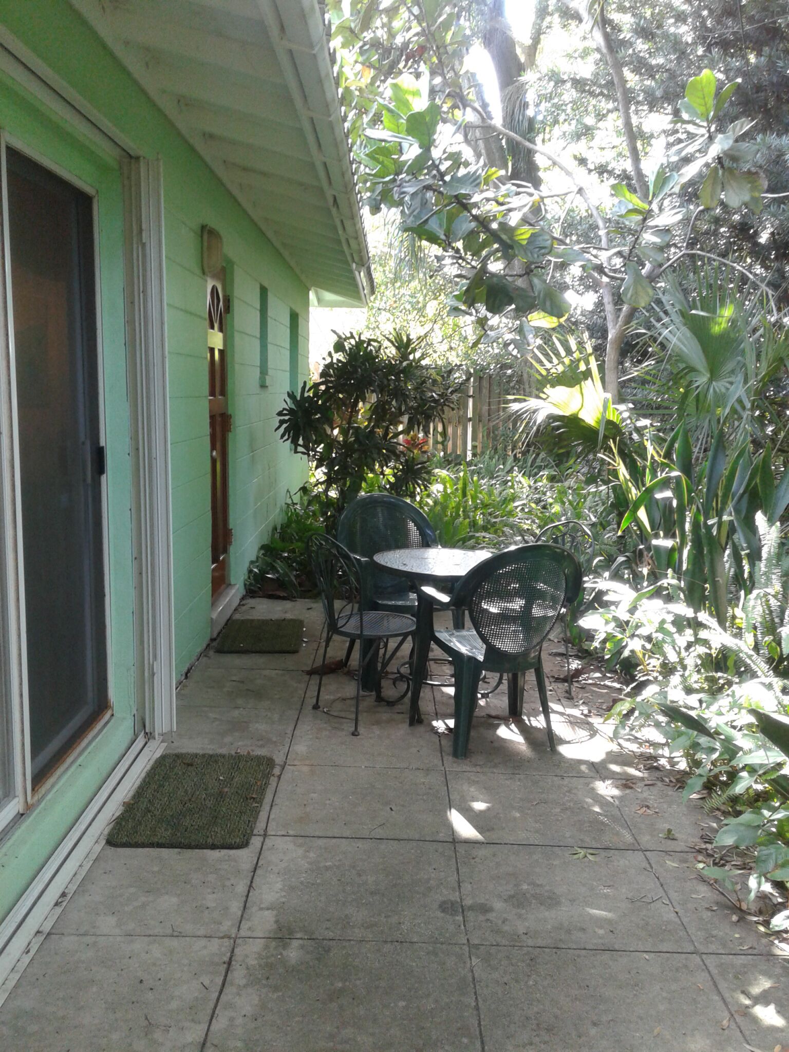 A patio with a table and chairs, surrounded by greenery.