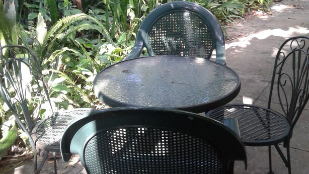 Ein Patio mit rundem Tisch und zwei Stühlen, umgeben von üppiger Bepflanzung und unterschiedlichen Pflanzen.