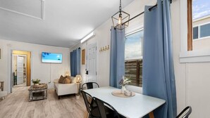 Moderni olohuone, jossa on ruokailutila, seinälle asennettu televisio ja suuri ikkuna, jossa on verhot.