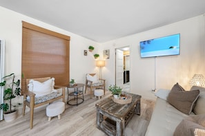 Un salon comprenant un canapé, des fauteuils, une table basse, un téléviseur et une fenêtre donnant sur un beau paysage.