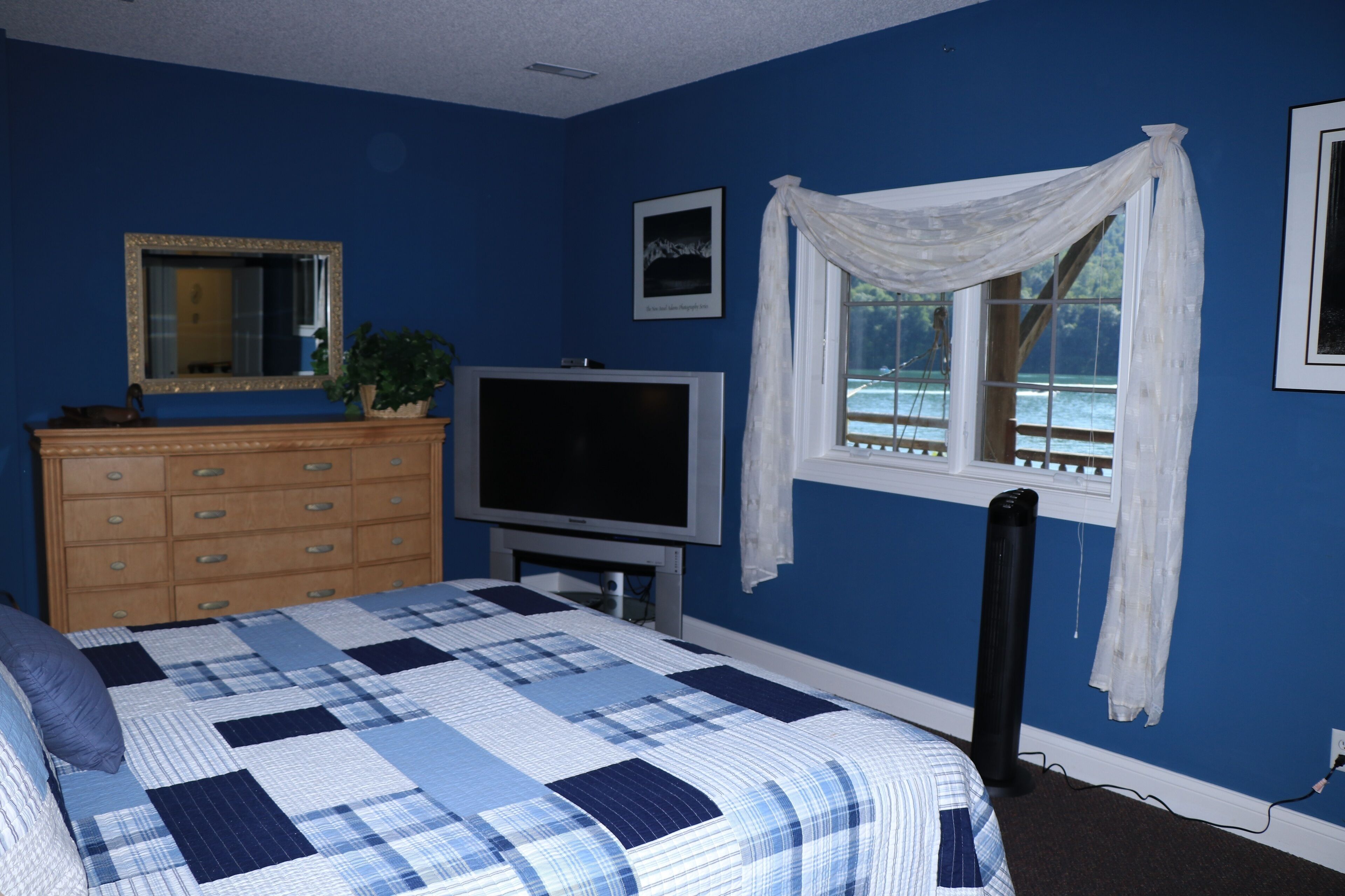 A bedroom with a bed, dresser, television, and a window with curtains.