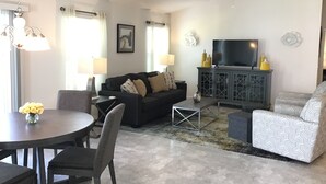 Een woonkamer met een bank, een televisie, een eettafel met stoelen en een plafondventilator.