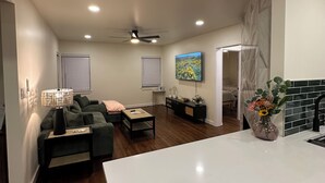 A modern living room with a sofa, coffee table, and a TV. There is a kitchen area with a white countertop and a vase of flowers. - Perfect Nest located in midtown, walk to the fairgrounds (Tulsa)
