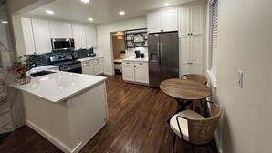 A modern kitchen with white cabinets, stainless steel appliances, and a wooden dining table. - Perfect Nest located in midtown, walk to the fairgrounds (Tulsa)
