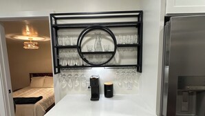 A compact kitchen with white cabinets, a stainless steel refrigerator, a coffee maker, and a wine glass display. - Perfect Nest located in midtown, walk to the fairgrounds (Tulsa)