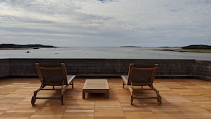 Una terraza con dos sillas de madera y una mesa, con vista a una masa de agua tranquila y tierra distante.