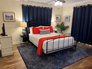 A neatly arranged bedroom with a bed, nightstands, a lamp, a plant, and a ceiling fan.