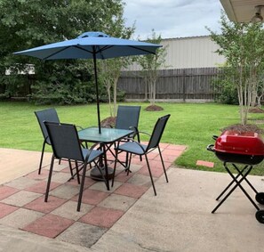 An outdoor patio with a table and chairs, a blue umbrella, and a barbecue grill.