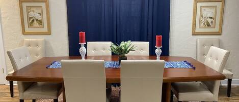 A dining room with a wooden table, four chairs, a blue curtain, and two wall-mounted light fixtures.